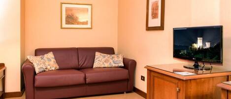 A living room with a brown sofa, two pillows, a wooden cabinet, and a framed picture on the wall.