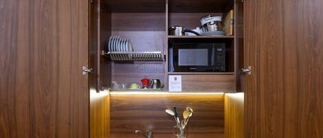 Una cocina equipada con microondas, un lavamanos y un hervidor de acero inoxidable.