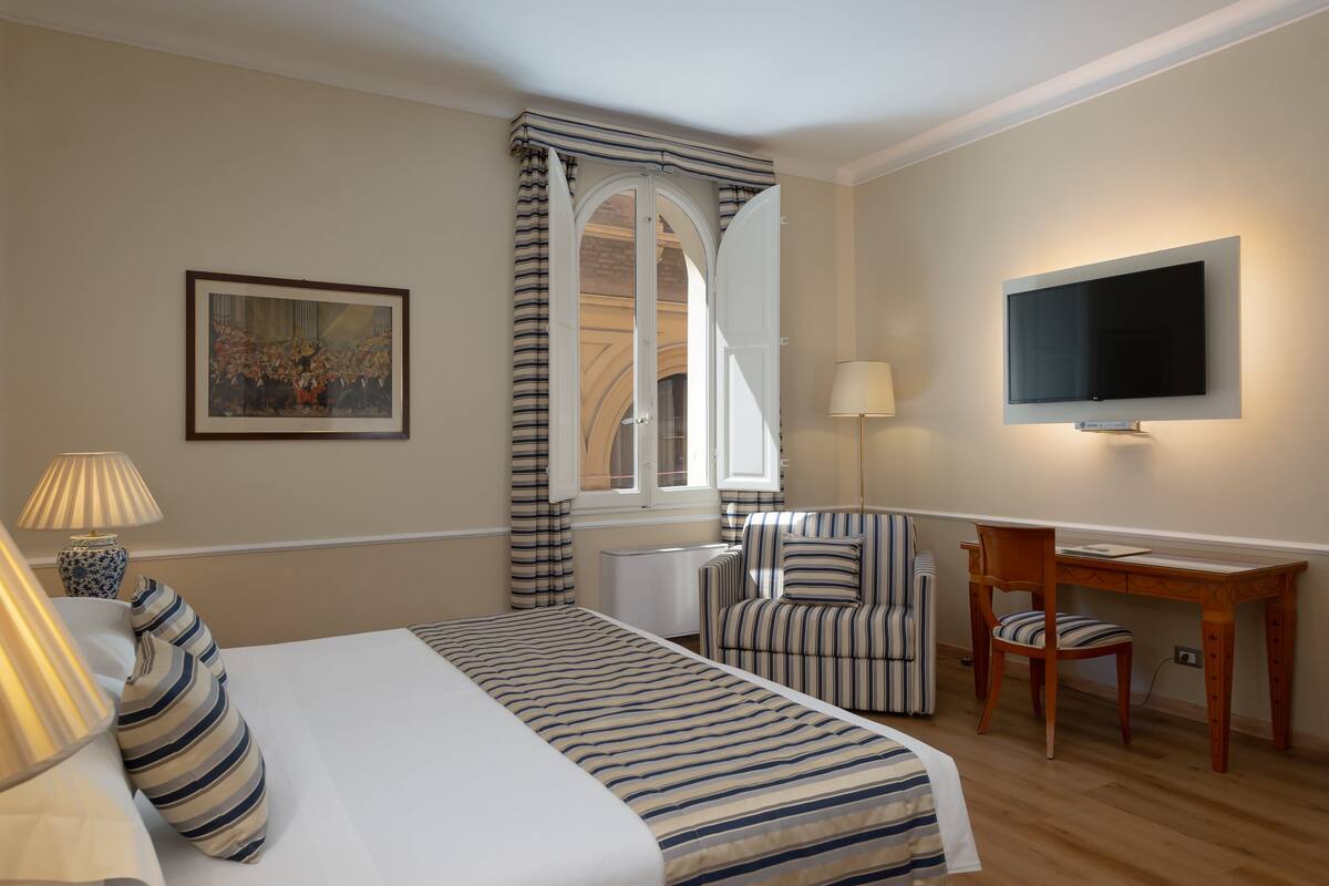 Ein Hotelzimmer mit einem Bett, einem Schreibtisch, einem Stuhl, einem Fernseher und einem Fenster mit Vorhängen.