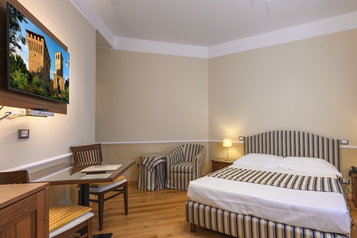 Ein Hotelzimmer mit Bett, Schreibtisch, Stuhl und einem an der Wand befestigten Fernseher.