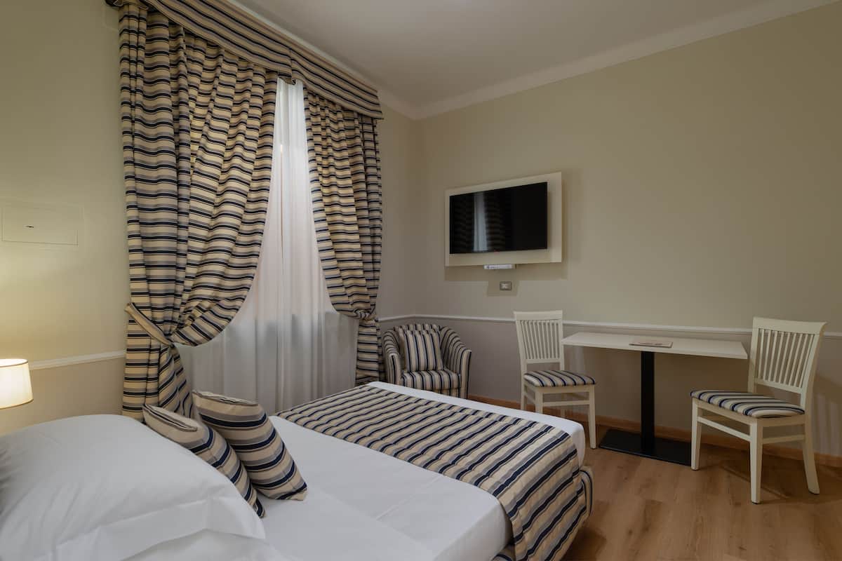 Ein Hotelzimmer mit Bett, zwei Stühlen, einem Schreibtisch, einem Fernseher und Vorhängen.