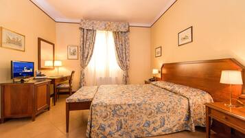 Quarto de hotel com cama, escrivaninha, cadeira e televisão.