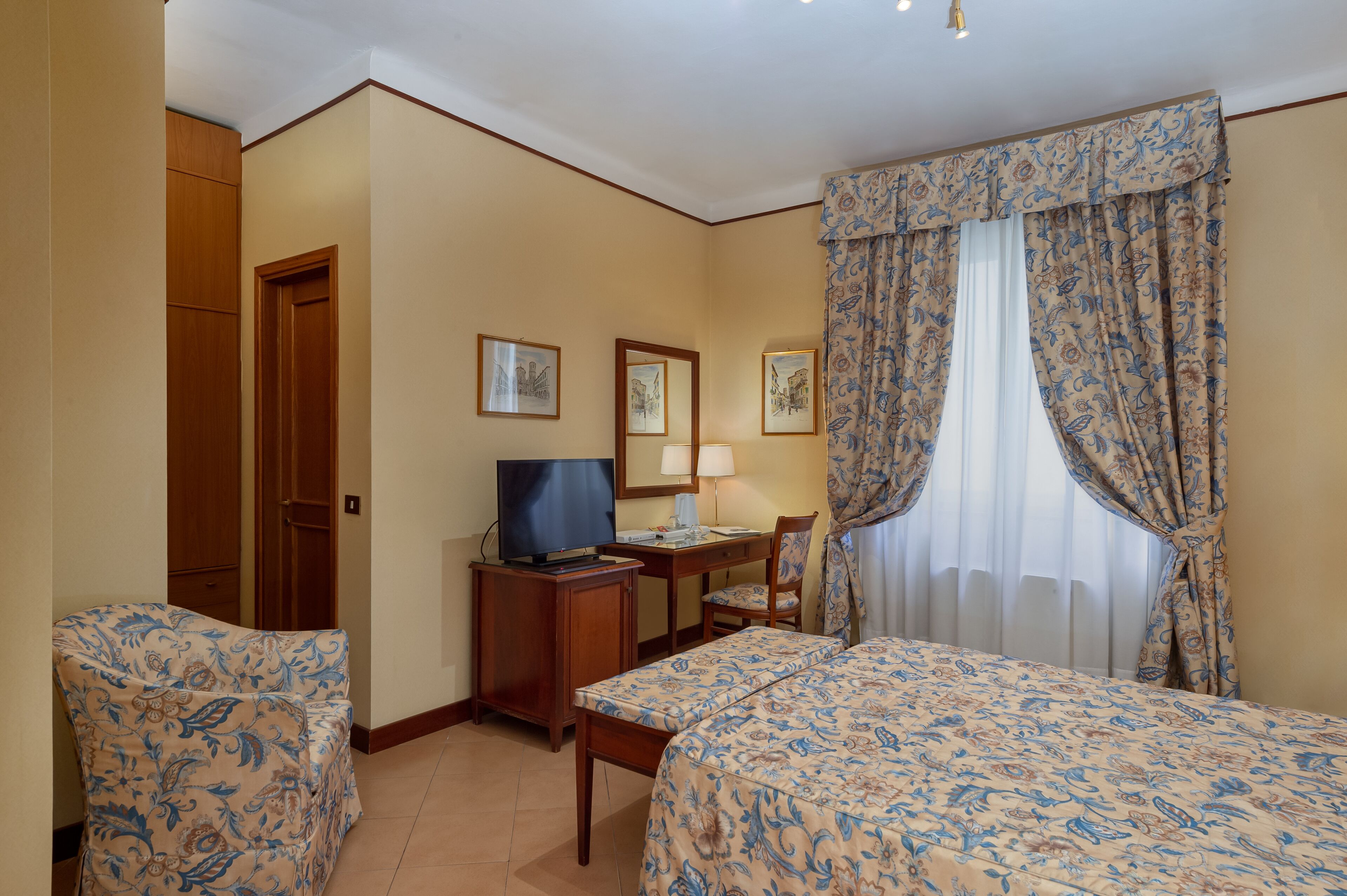 A hotel room with two beds, a desk with a TV, a chair, and a wardrobe.