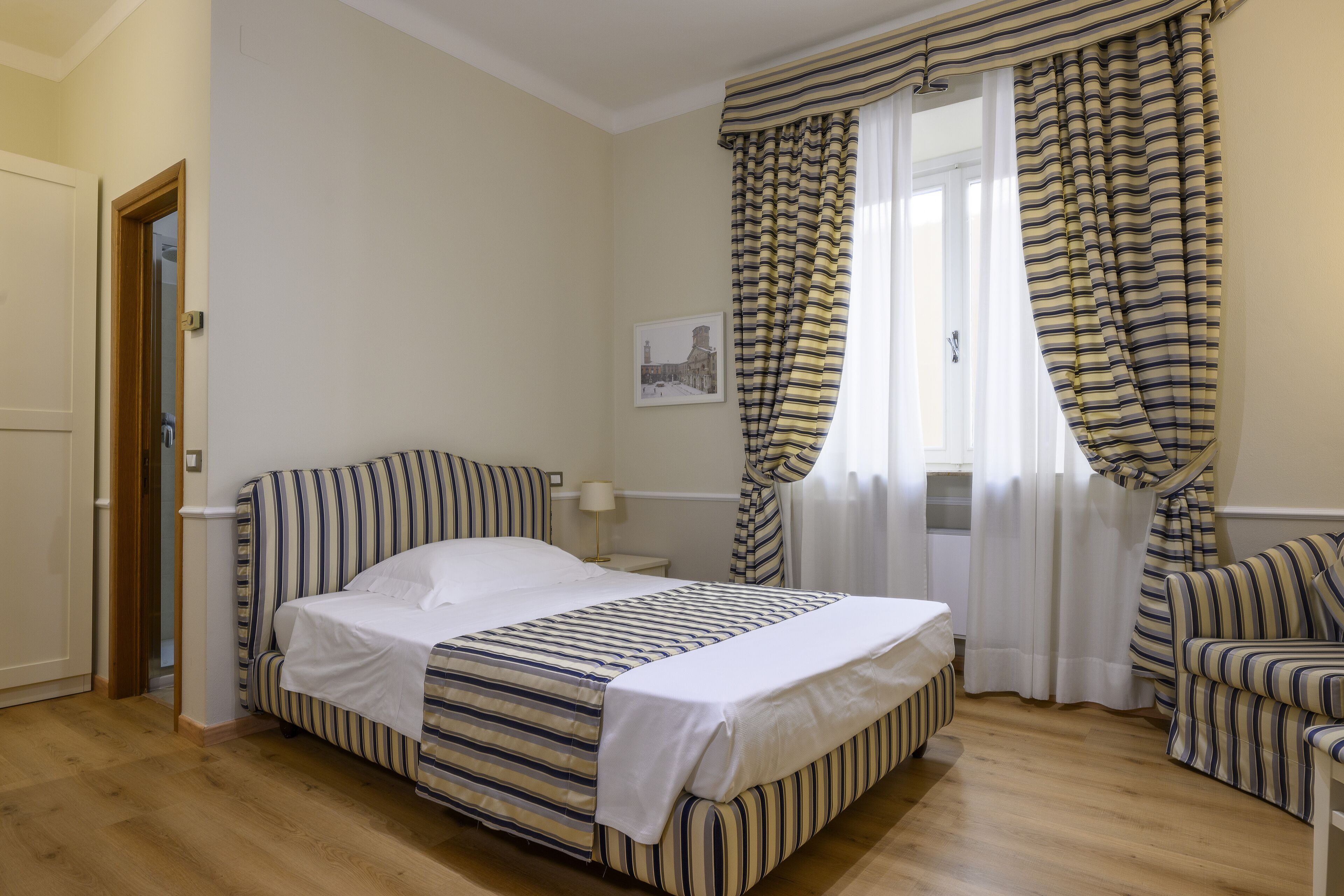 A bedroom with a bed, a chair, a window with curtains, and a door.