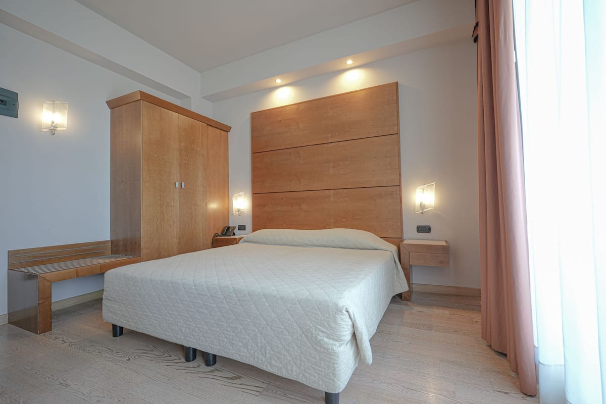 A bedroom with a bed, wooden wardrobe, bedside tables, and wall-mounted lights.