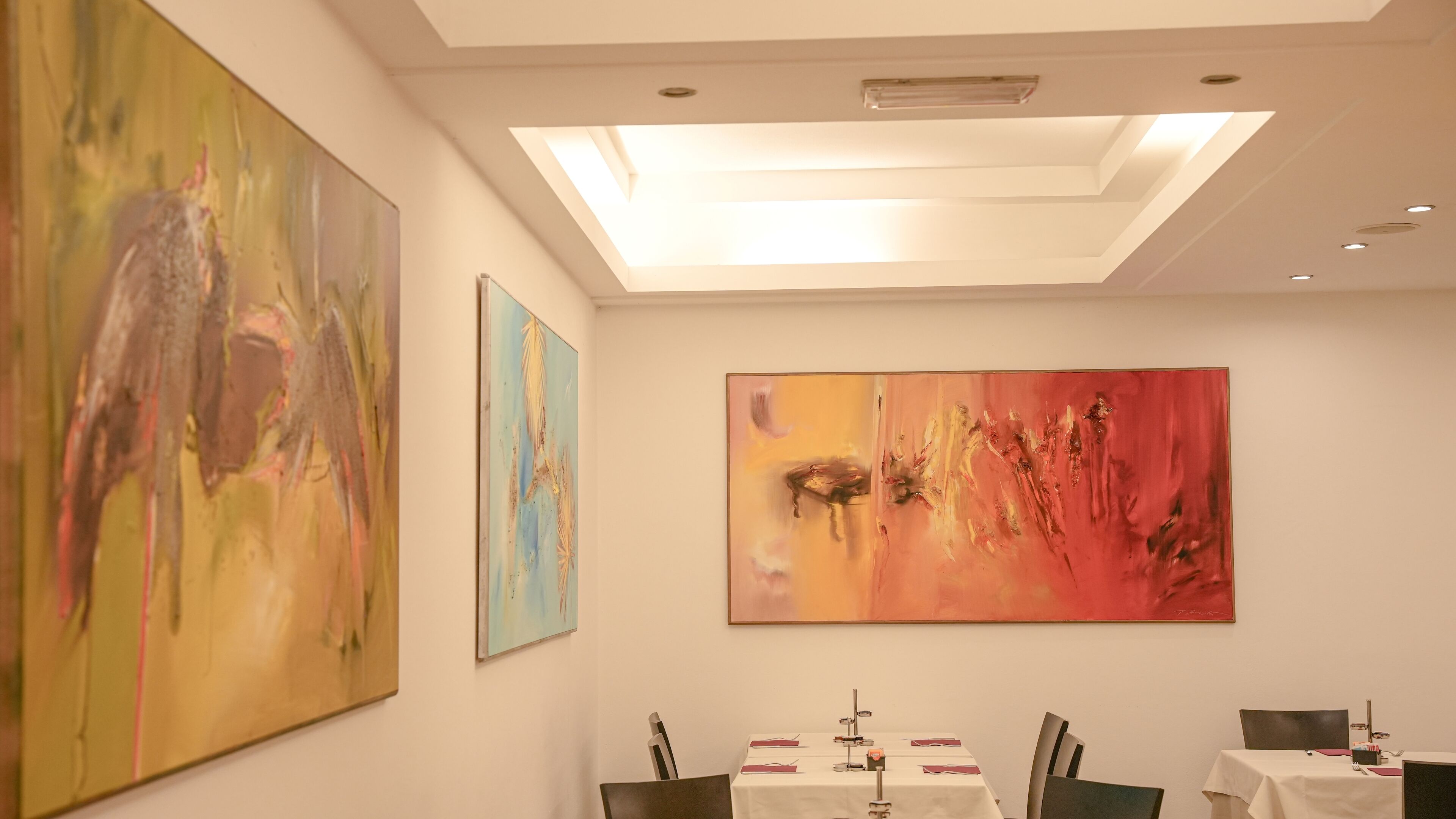 Un espace repas agrémenté d’œuvres d’art abstraites sur les murs, une table dressée pour deux personnes et une lucarne au plafond.