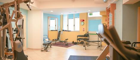 Ein Fitnessraum mit Trainingsgeräten, einem Fenster und einer Uhr an der Wand.