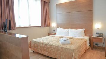 Een hotelkamer met een bed, nachtkastjes, een bureau en een raam met gordijnen.