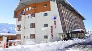 Ein modernes Hotel mit weißer Fassade und orangefarbenen Akzenten, das ein Skisymbol und den Schriftzug 'SUD OUEST' zeigt.