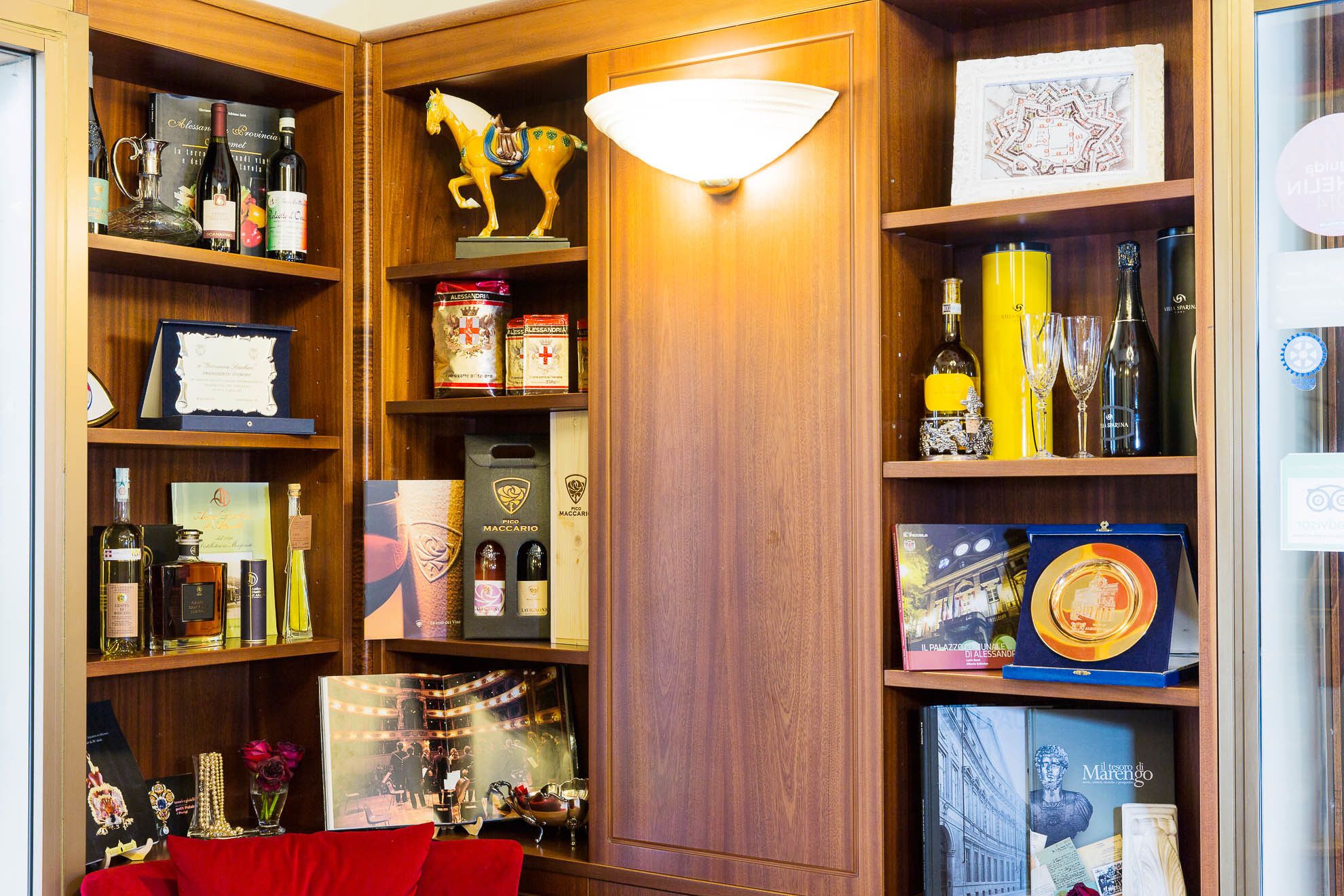 A well-organized wine and spirits collection in a wooden cabinet with a decorative horse figurine, framed certificates, and a glass display case.
