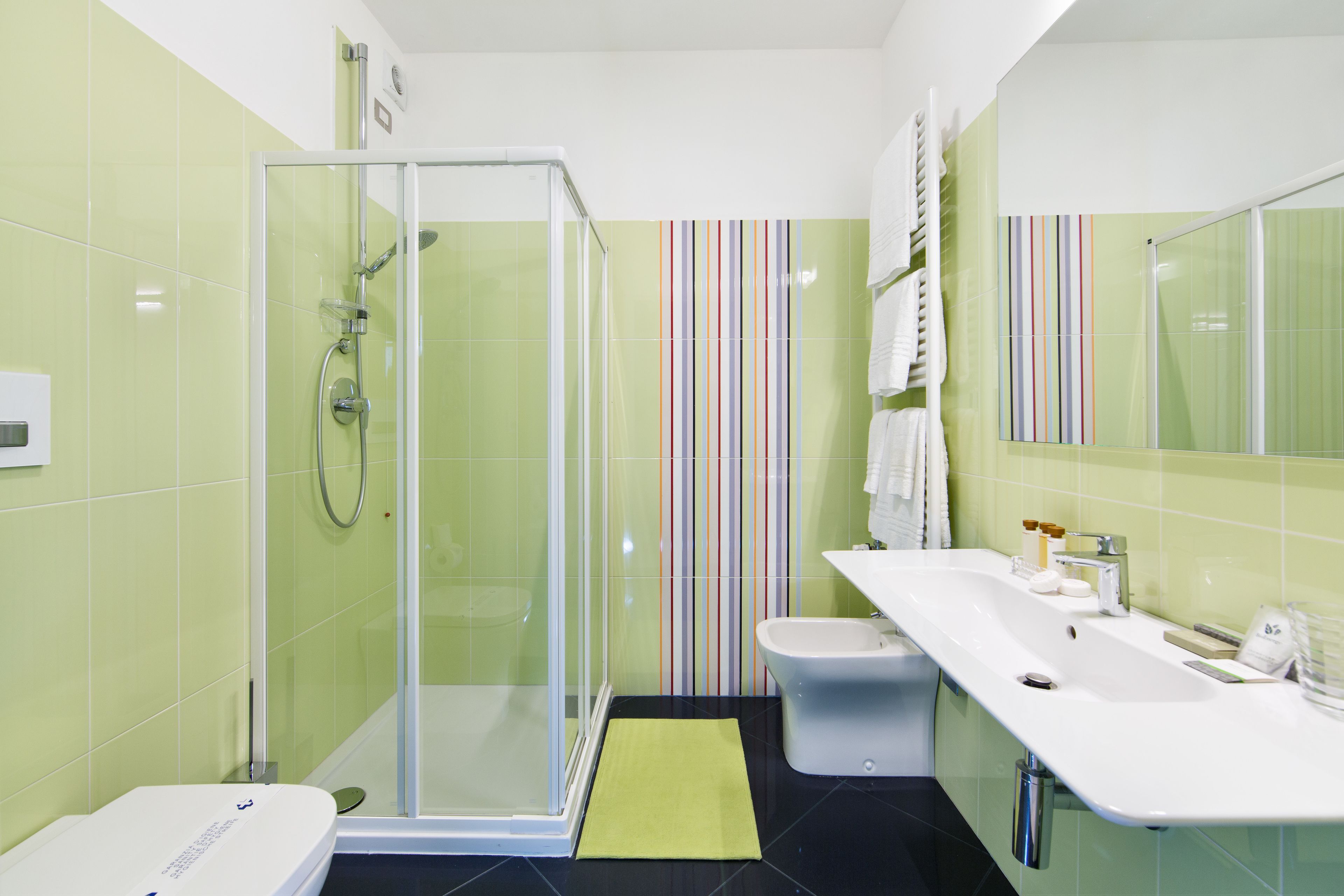 Un baño moderno con ducha envuelta en vidrio, un lavabo blanco y un diseño de pared a rayas.