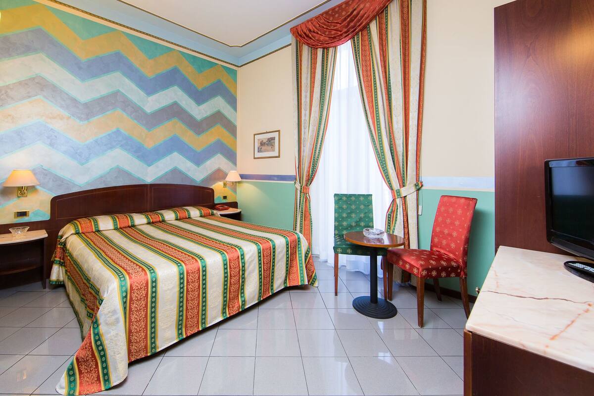 Ein Hotelzimmer mit Bett, Fernseher, Stuhl, Tisch und Wanddekoration.