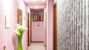 A hallway with pink walls, a wooden door, and a vase with white flowers. - Hotel Londra (Alessandria)