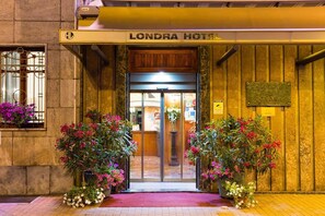 La entrada al Hotel Londra, con fachada de madera, puerta de cristal y plantas en macetas a ambos lados.