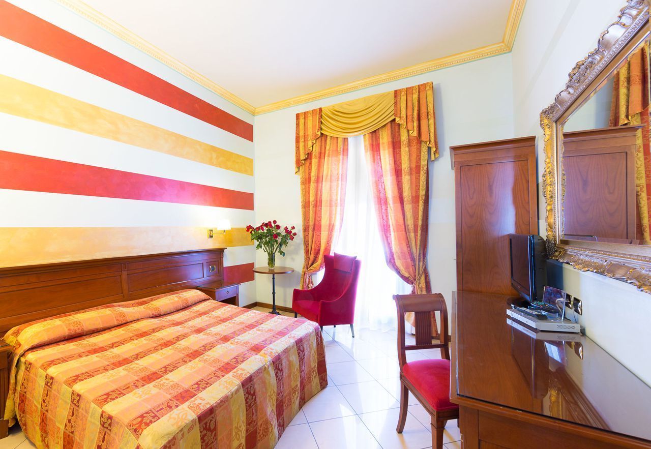 Una habitación de hotel con una cama grande, un escritorio con computadora, una silla y un televisor.