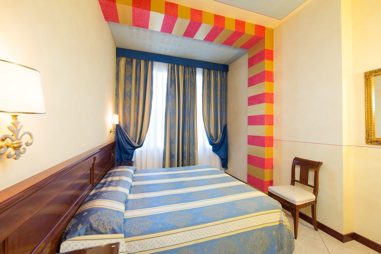 A hotel room with a bed, a chair, a lamp, and a mirror on the wall.