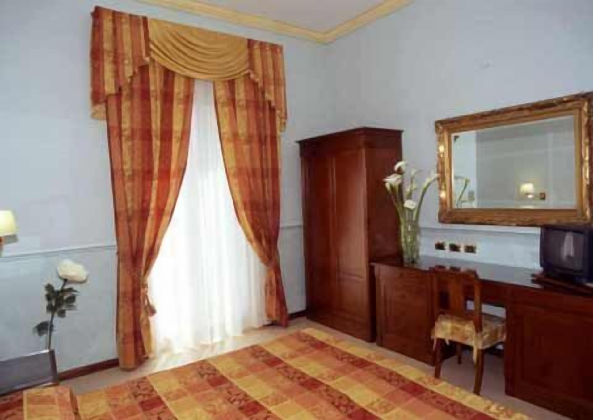Ein Zimmer mit großem Fenster, einem Holztisch, einem Spiegel und einem gemusterten Teppich.