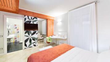 Habitación de hotel con cama, escritorio, silla, espejo y baño visible a través de una puerta abierta.
