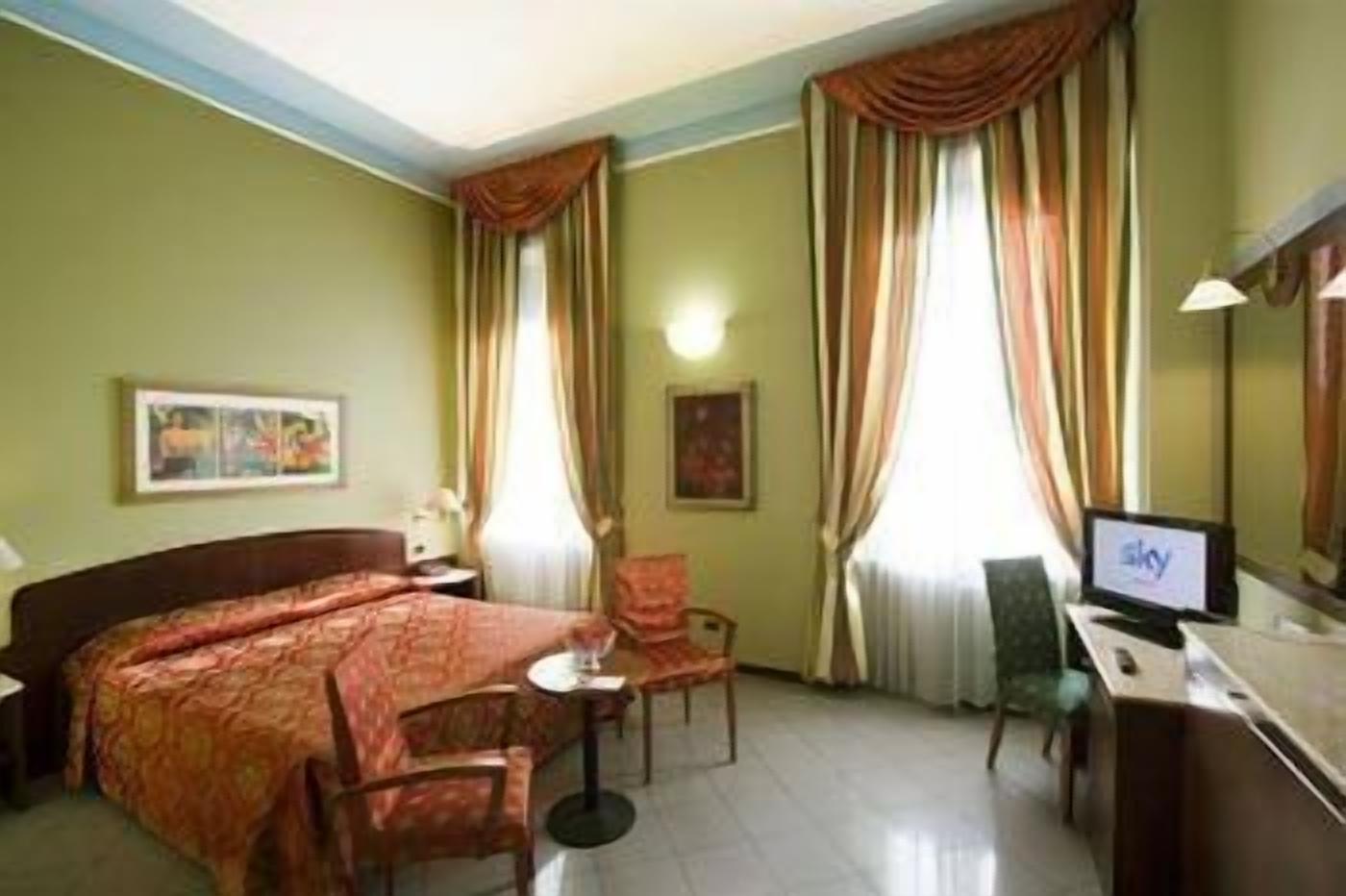 Una camera d'albergo con un letto, una scrivania con un computer, una sedia e tende.