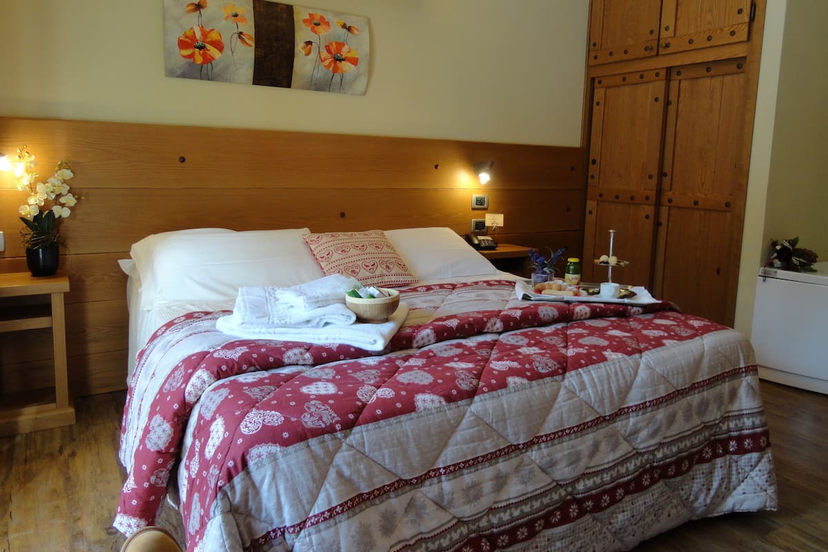 A neatly made bed with a red and white patterned bedspread, a wooden headboard, and a wall-mounted painting of flowers.