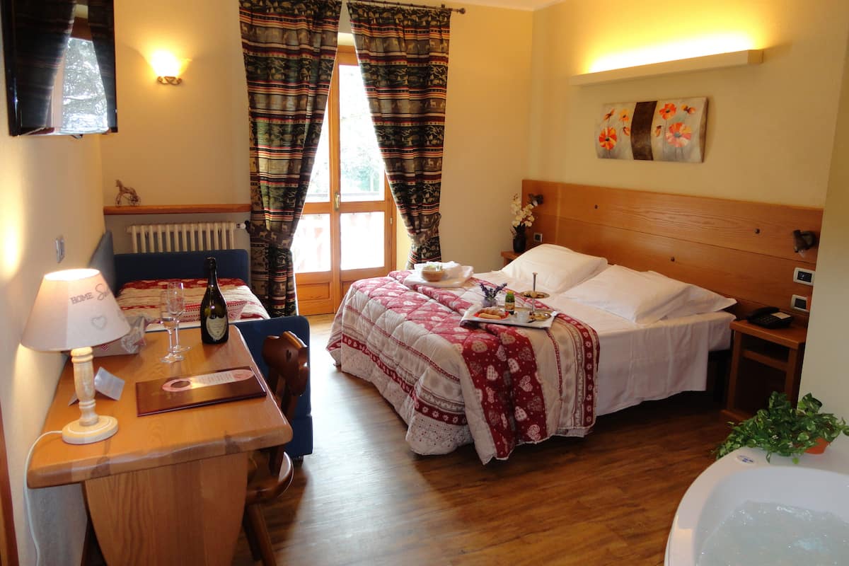 A hotel room with a bed, bedside table, lamp, and a view of the outdoors through the window.