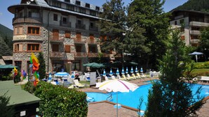 Un hotel con zona de piscina, mobiliario exterior y montañas al fondo.
