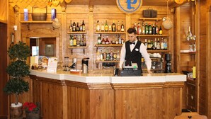 Una zona de bar con barra, estantes llenos de botellas, una caja registradora y una mesa pequeña.