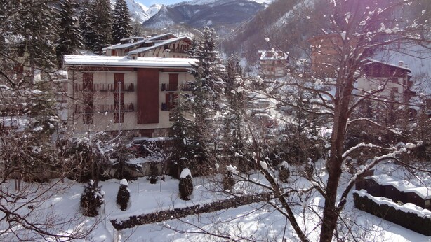 Un hotel con fachada roja, rodeado de árboles nevados y montañas al fondo.
