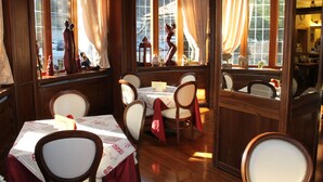 Un comedor con mesas y sillas de madera, ventanas amplias con cortinas y vistas al exterior.