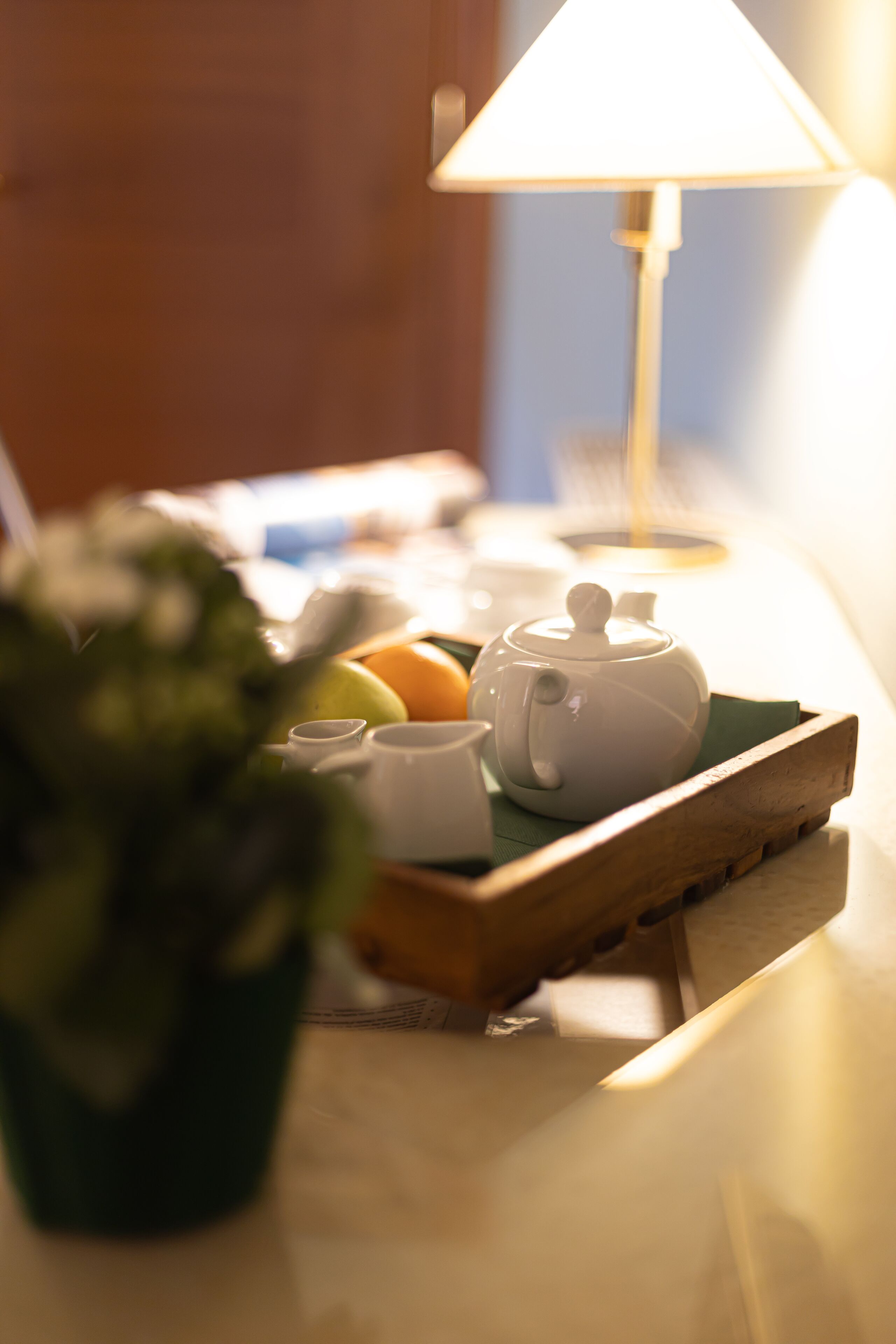 A table with a teapot, cups, and fruits under a lamp.