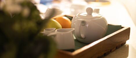 A table with a teapot, cups, and fruits under a lamp.