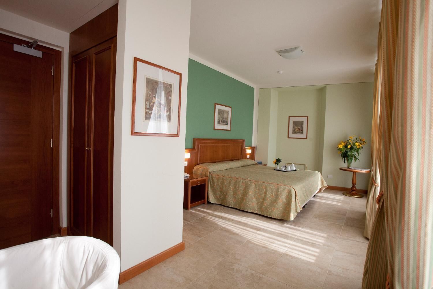 A hotel room with a bed, a nightstand, a chair, and a small table with flowers.
