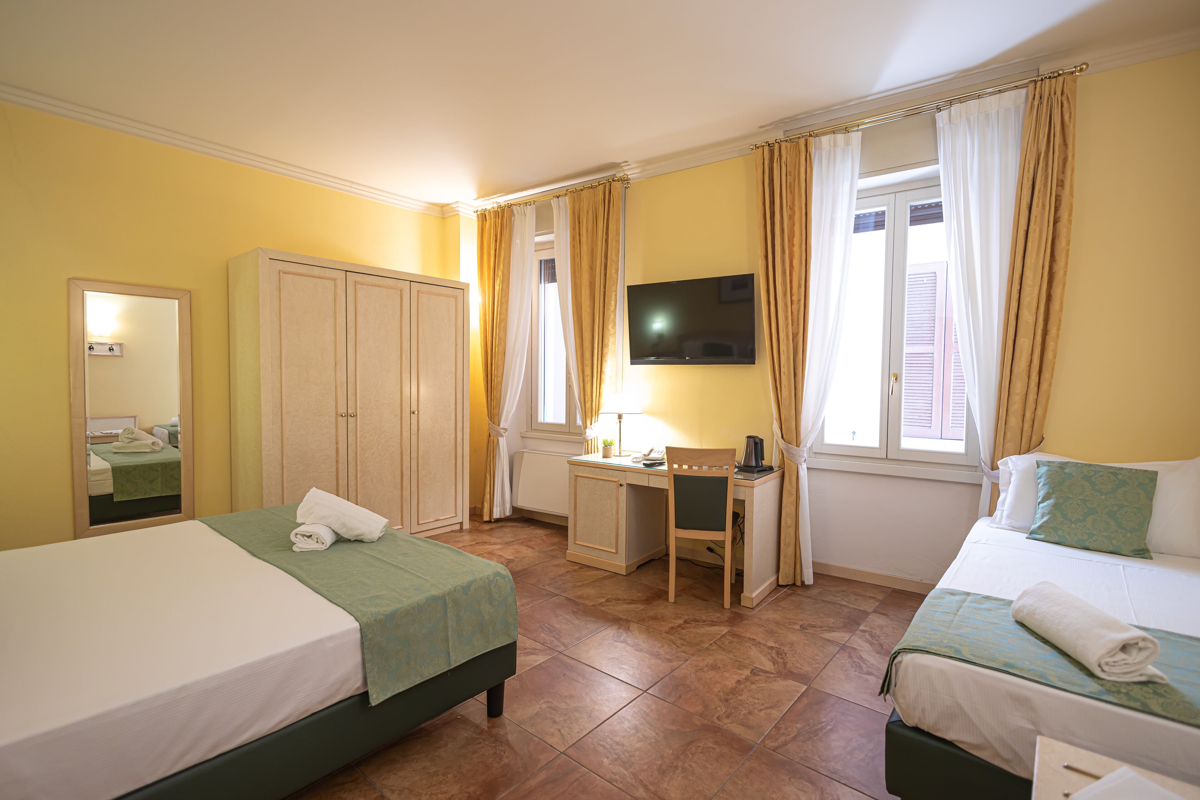 A hotel room with two beds, a desk, a chair, a television, and a window with curtains.