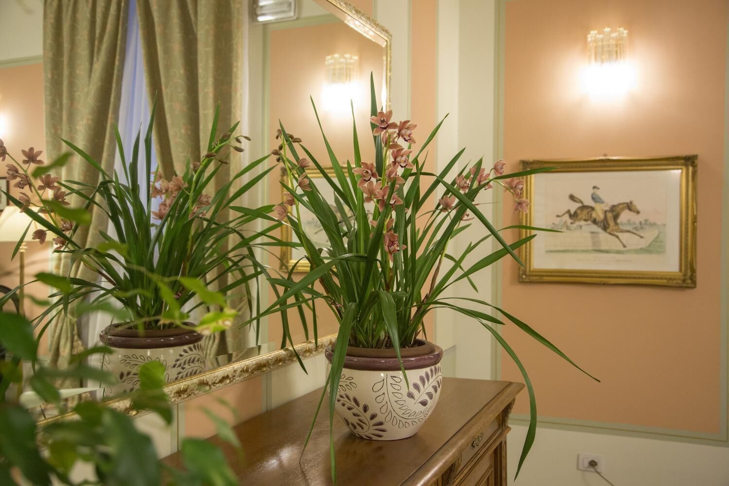 Une pièce avec un miroir qui reflète une plante en pot et un tableau encadré accroché au mur.