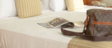 A neatly made bed with white bedding and striped pillows, a framed picture on the wall, and a brown bag on the bed.