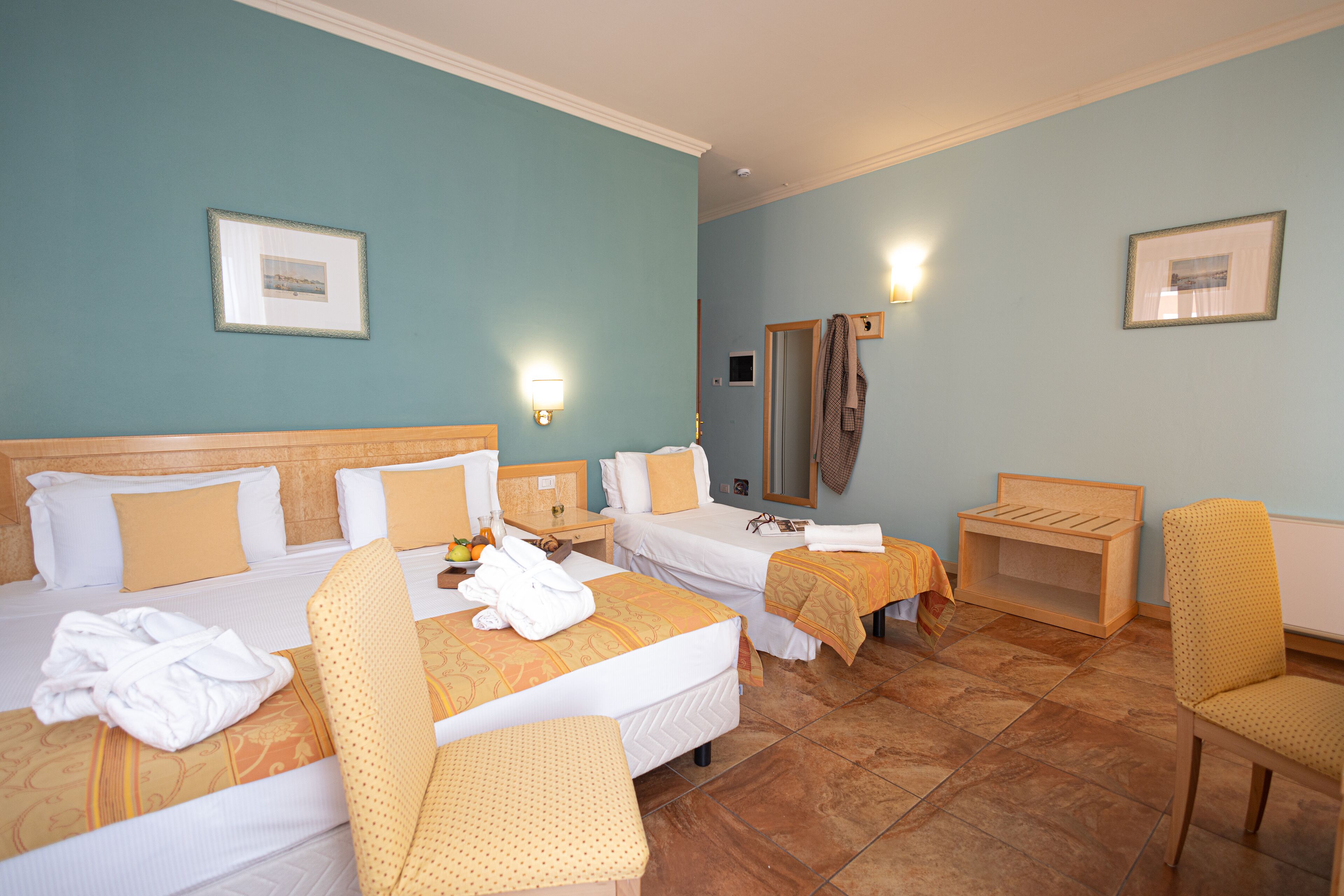 Ein Hotelzimmer mit zwei Betten, einer Sitzecke inklusive Stuhl, einem kleinen Tisch und einem Spiegel.