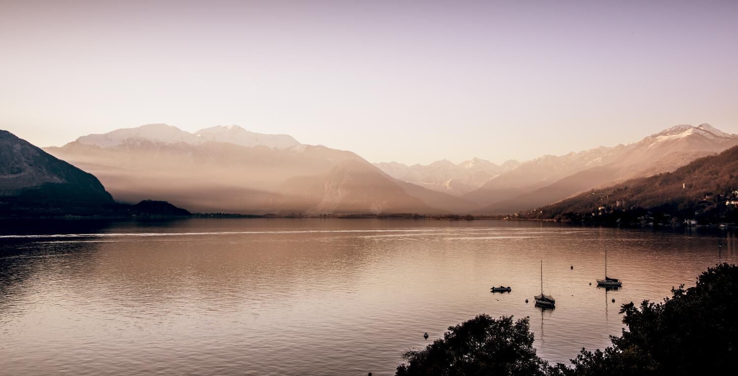 Un lago sereno con barcos, rodeado de montañas y una atmósfera brumosa.