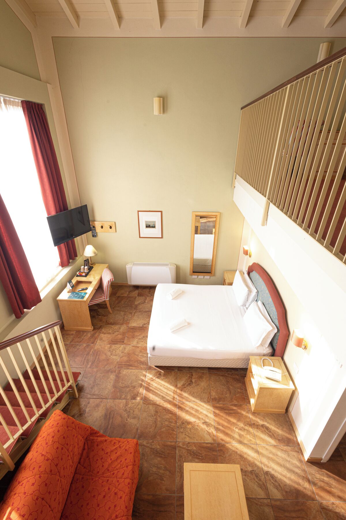 A hotel room with a bed, a desk, a chair, a TV, a mirror, and a window with curtains.
