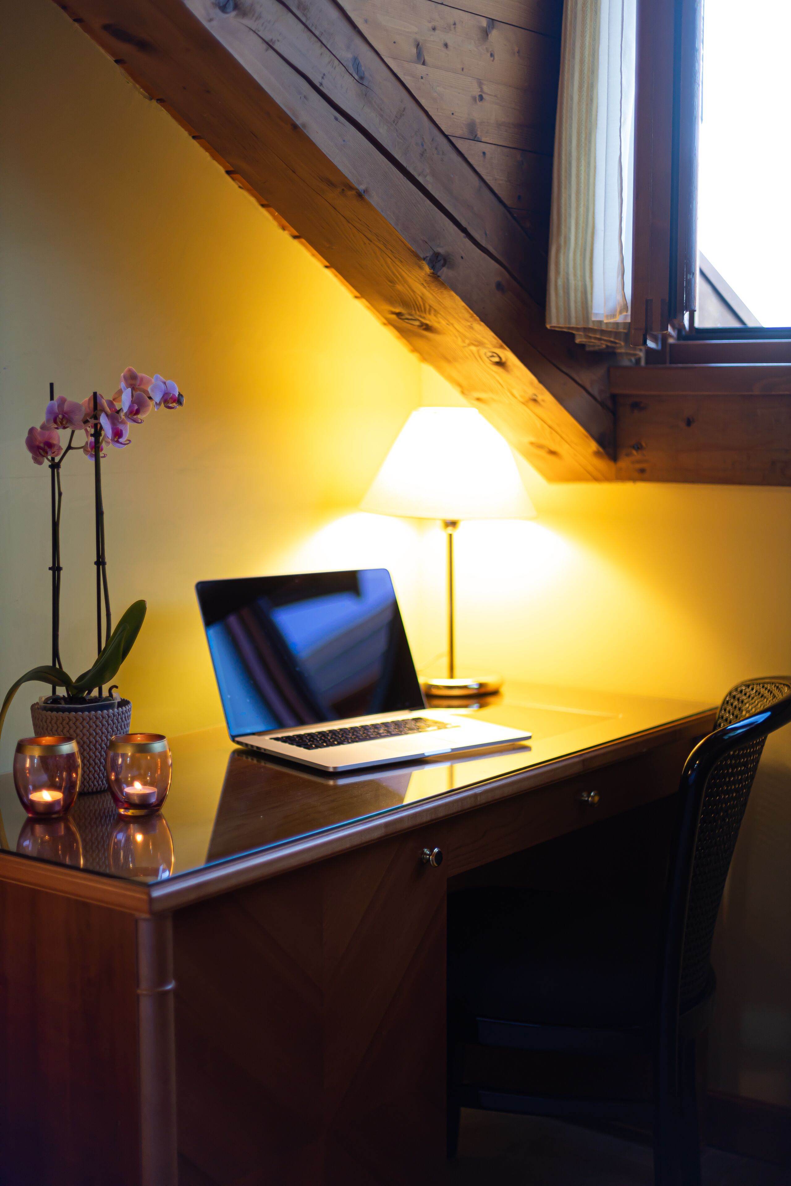 A wooden desk with a laptop, a lamp, and a potted orchid.
