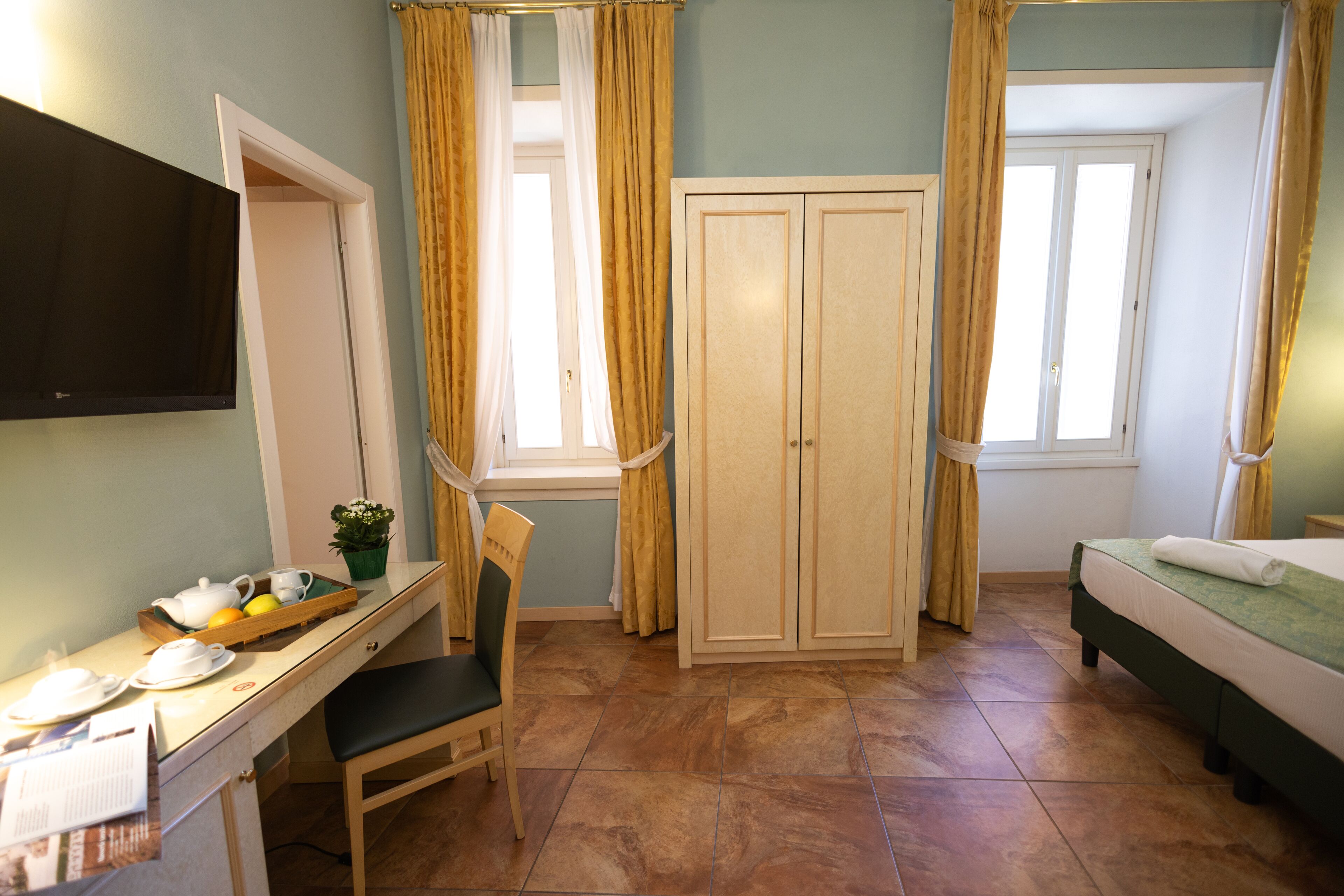 A hotel room with a bed, a desk with a chair, a wardrobe, and a television.