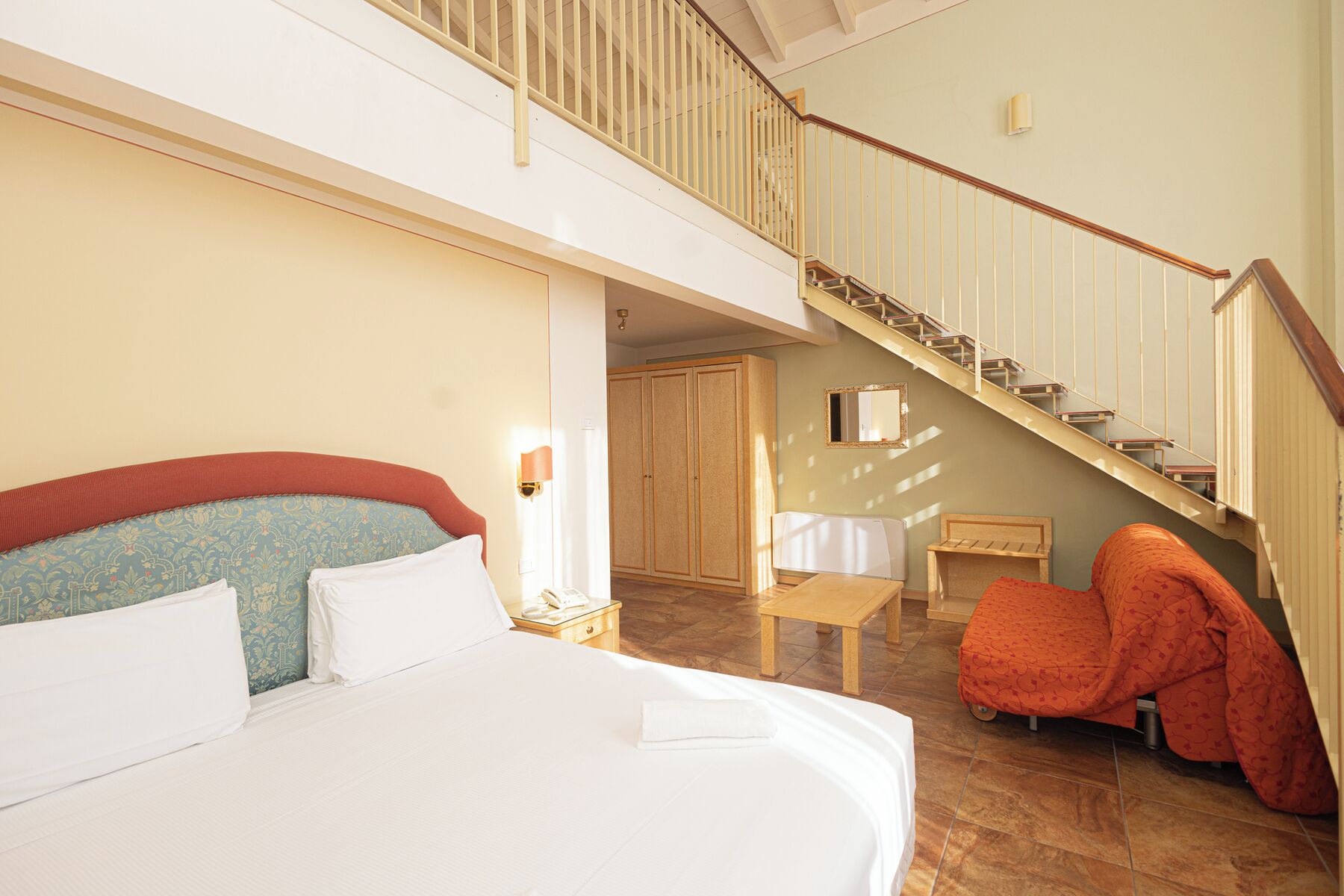 Camera d'albergo con un letto grande, un tavolino, una sedia e una scala.