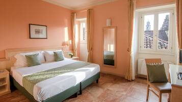 Une chambre d’hôtel avec un lit, une chaise, un bureau, une fenêtre donnant sur des immeubles et un tableau encadré au mur.