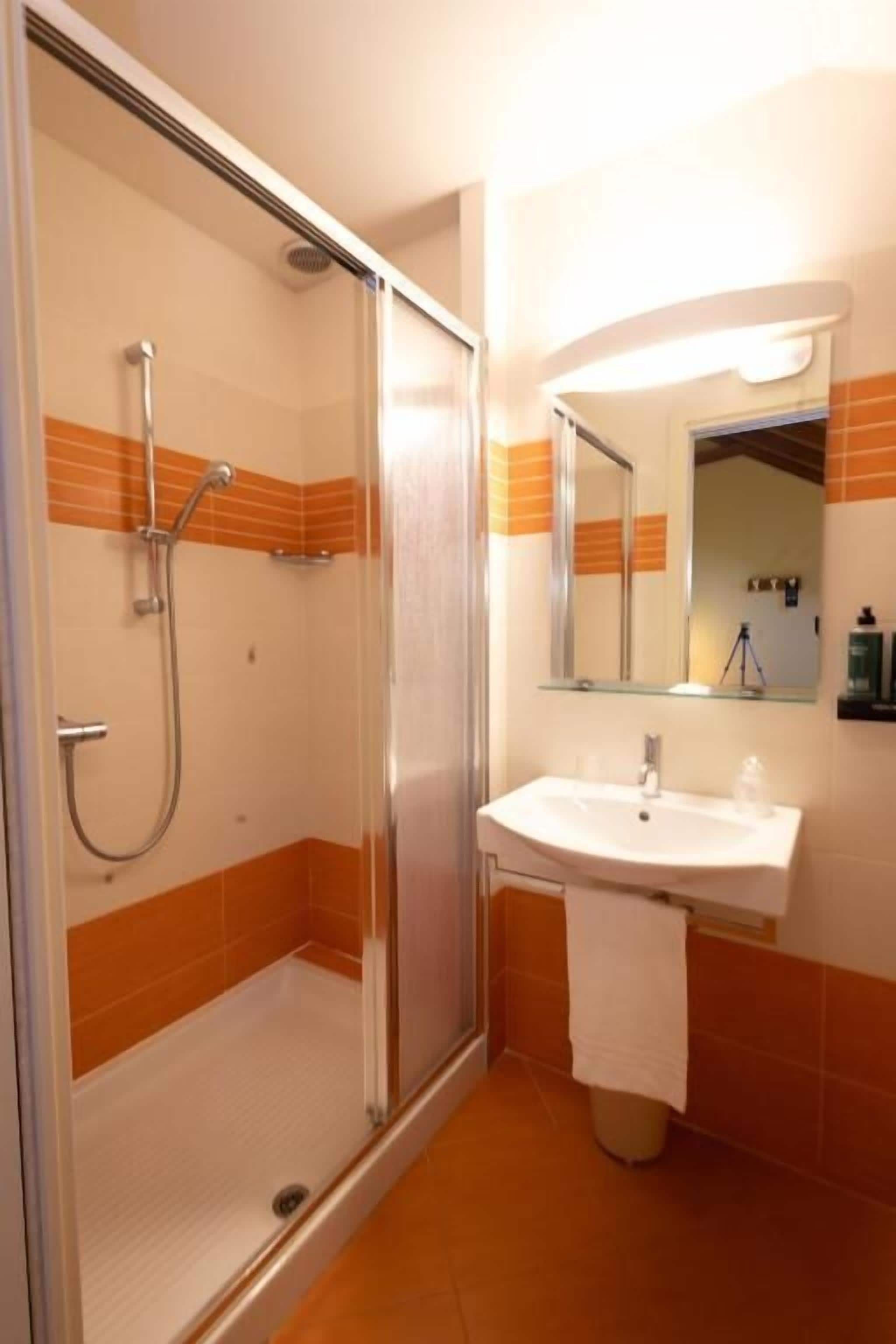 Een badkamer met een douche met glazen wand, een wit wastafelmeubel en oranje betegelde muren.