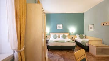 A hotel room with two beds, a wooden chair, a small table, and a window with curtains.