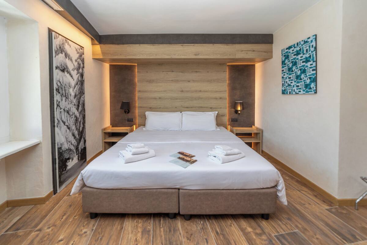Una habitación de hotel moderna con una cama grande, cabecera de madera y dos mesitas de noche con lámparas.