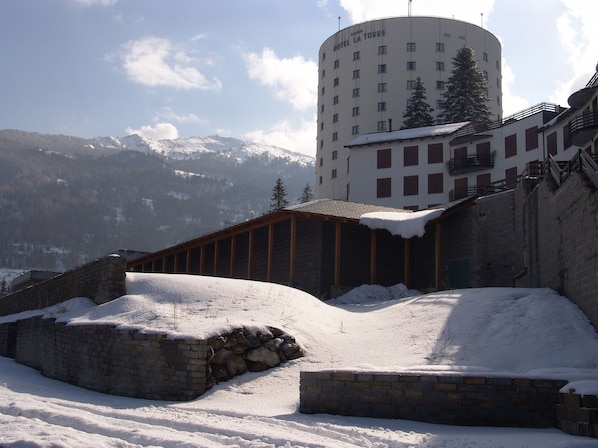 A snow-covered building with a stone wall and a wooden structure in the foreground. - Hotel La Torre (Sauze d'Oulx)