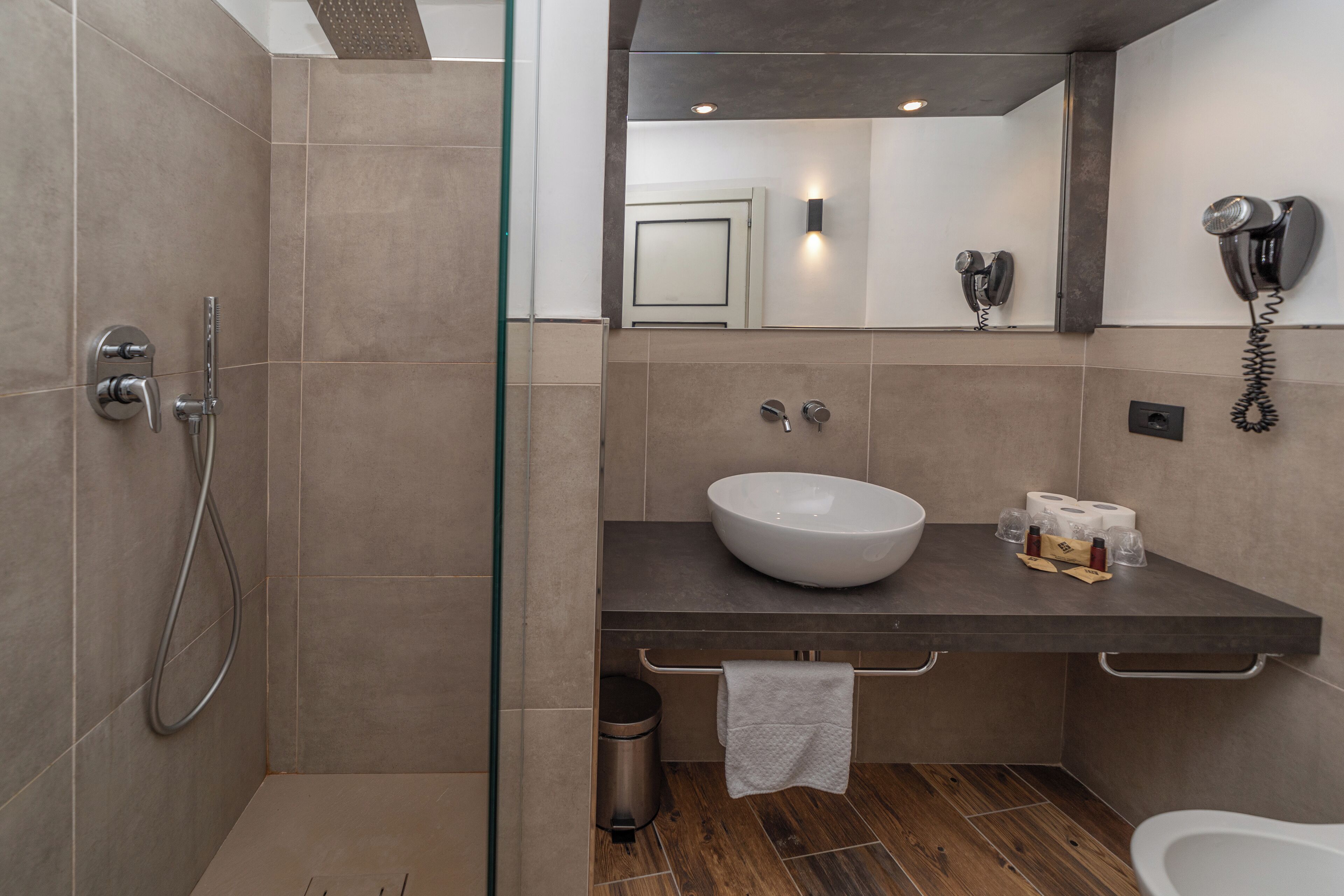 A modern bathroom with a glass shower enclosure, a vessel sink, and a hairdryer mounted on the wall.