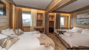 Habitación de hotel con dos camas, vigas de madera, chimenea y ventana con vistas a montañas nevadas.