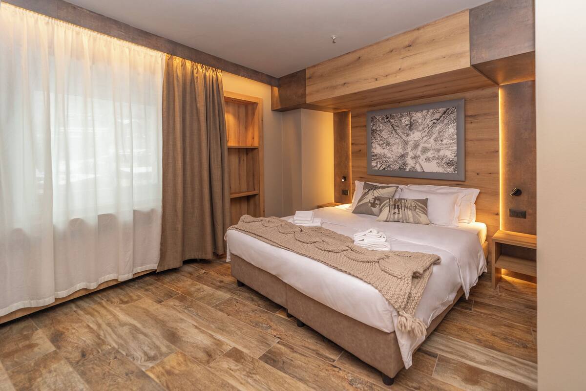 Un dormitorio con una cama grande, suelo de madera, cabecero de madera, una mesita de noche y una obra de arte colgada en la pared.