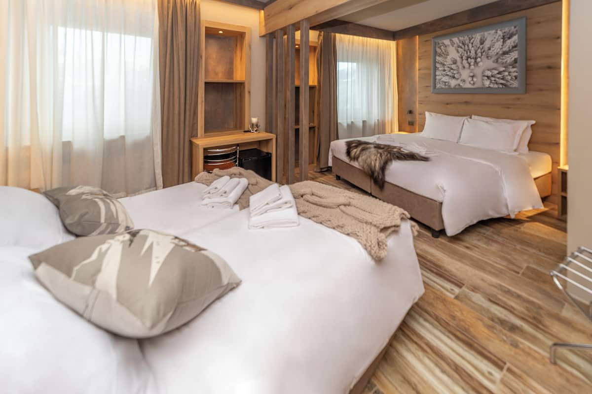 Habitación de hotel con una cama grande, una cama más pequeña, suelo de madera y un cuadro en la pared.